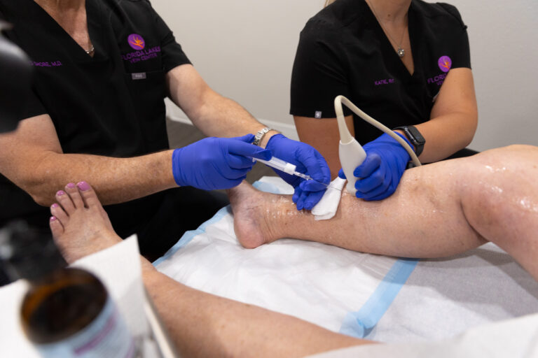 Two providers wear scrubs and medical gloves while they perform a varicose vein treatment near Longboat Key.