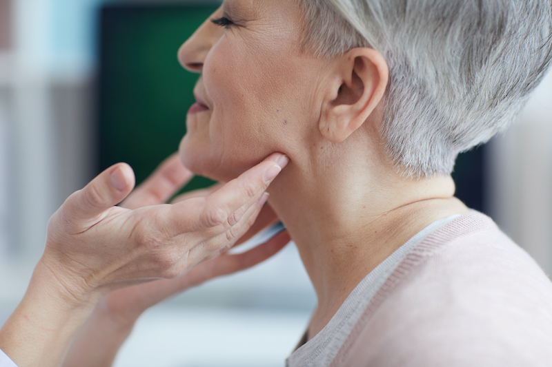 A doctor's hands checking the lymph nodes on a mature woman's neck as part of lymphedema treatment in Sarasota